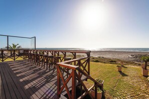 A wooden deck with outdoor seating overlooking a beach. - Burning Shore Hotel (Walvis Bay)