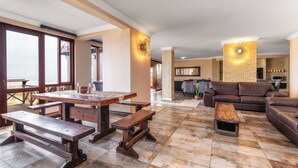 Amplia sala de estar con una mesa de madera y bancos, un sofá de cuero marrón y un pilar de piedra con una lámpara.