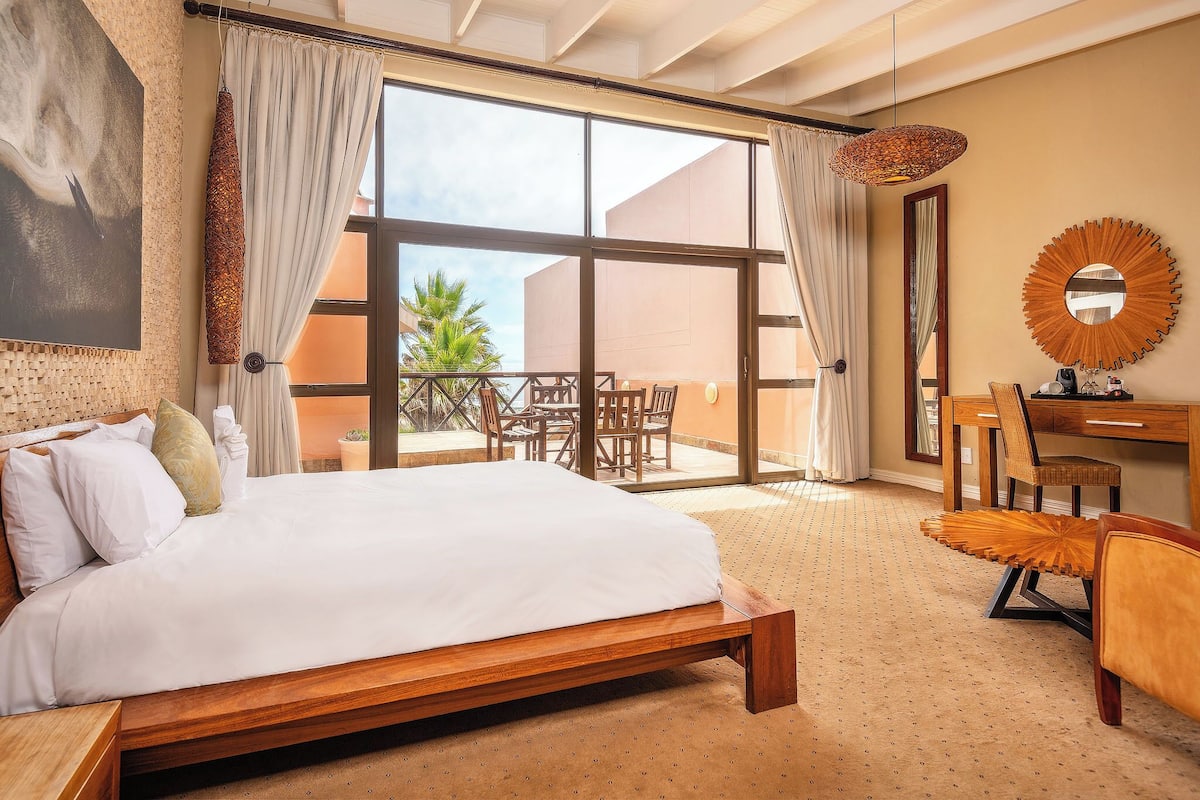 Un dormitorio con una cama grande, un escritorio, una silla, un ventanal y vistas al exterior.