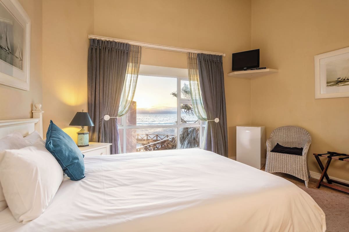 Una habitación de hotel con cama, televisión, sillón y vista al mar.