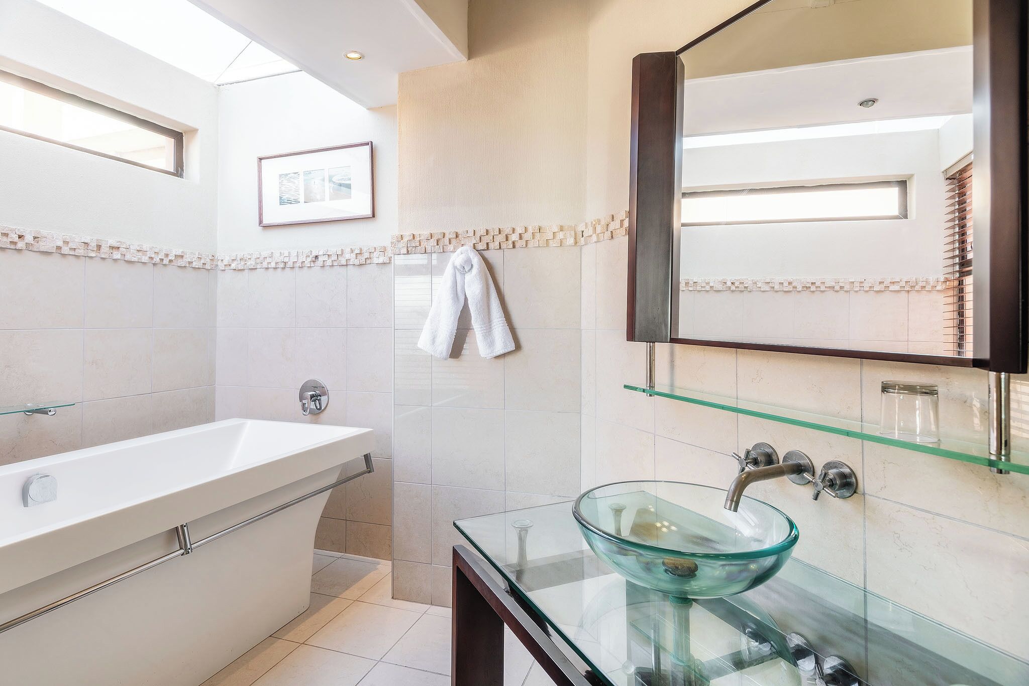 Un baño moderno con un lavamanos con cerramiento de vidrio, una bañera independiente y un espejo grande.