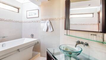Un baño moderno con un lavamanos con cerramiento de vidrio, una bañera independiente y un espejo grande.