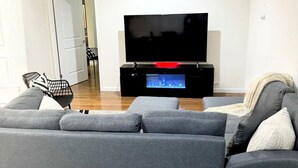 A modern living room with a grey sofa, a flat-screen TV on a black stand, and a small pool table. - Posh 2BR/2BA King Bed! Free Parking! 30 Min to NYC

 (East Orange)