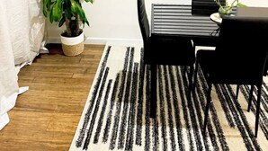 A room with a black table and chairs, a potted plant, a striped rug, and a window with blinds. - Posh 2BR/2BA King Bed! Free Parking! 30 Min to NYC

 (East Orange)