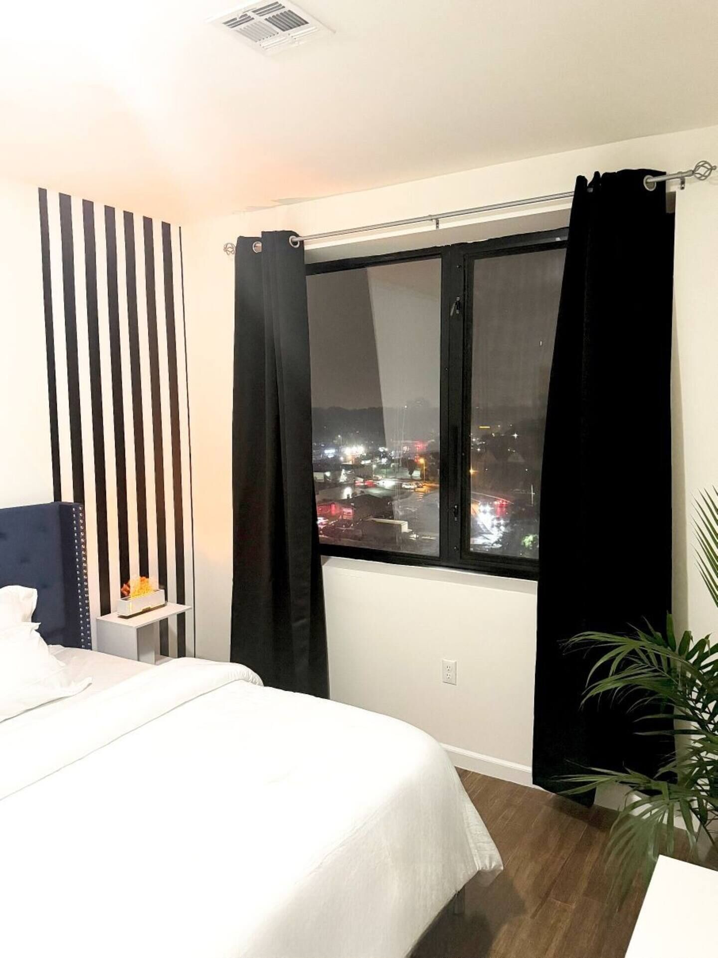Une chambre d’hôtel avec un lit, une table de chevet, une fenêtre avec des rideaux noirs et une vue sur le paysage urbain la nuit.