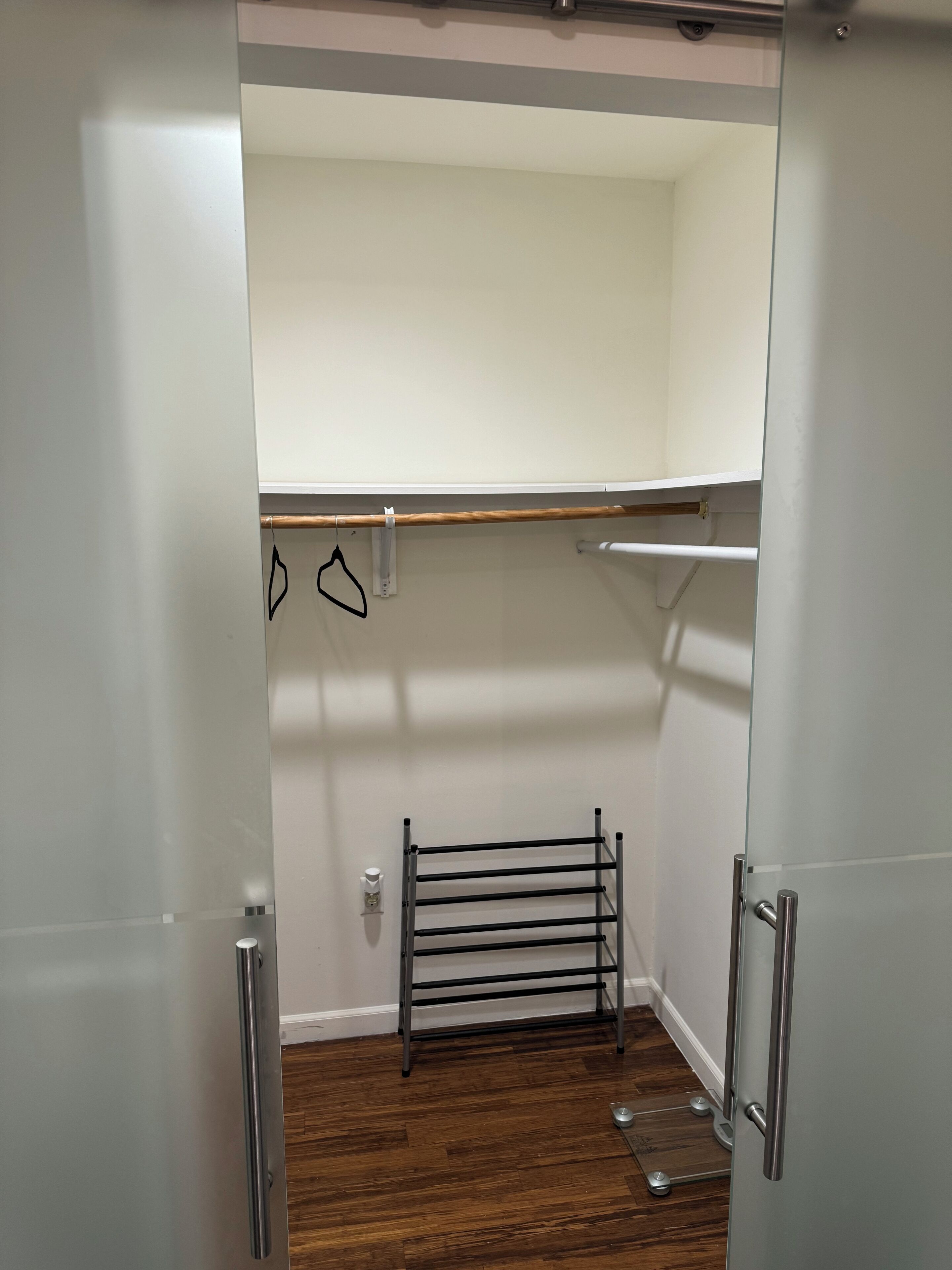 Un vestidor con un tendedero de metal, una pared blanca y suelo de madera.