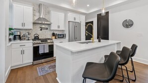 Une cuisine moderne avec des meubles blancs, des appareils en acier inoxydable, un îlot central doté de tabourets et un éclairage suspendu.