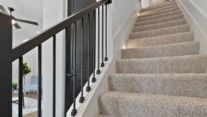 Un escalier avec une rampe noire, des marches recouvertes de moquette et une porte en haut.