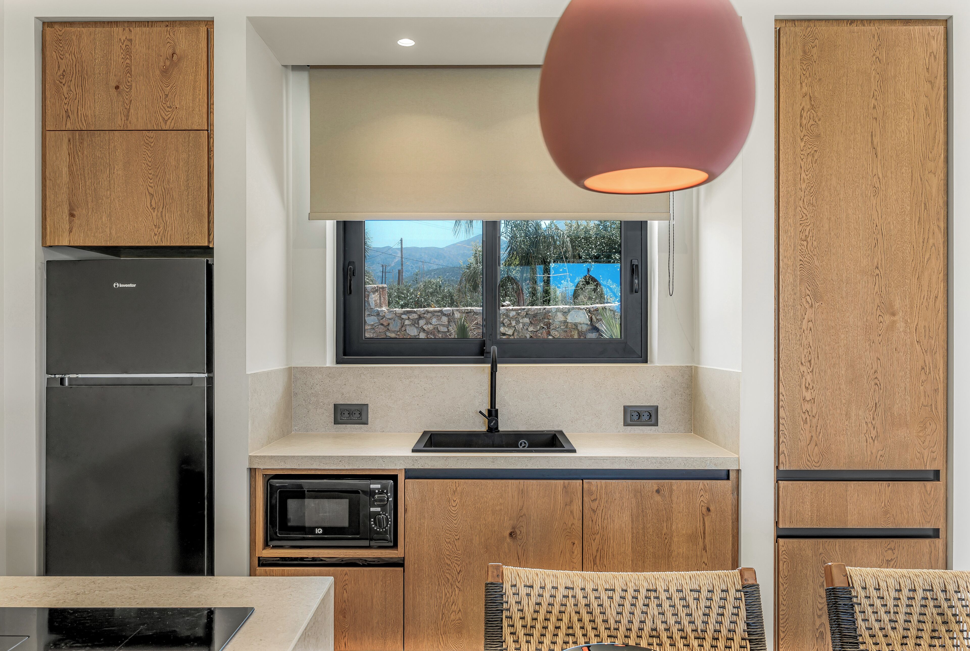 A modern kitchen with wooden cabinets, a black refrigerator, a microwave, and a window with a view of mountains.