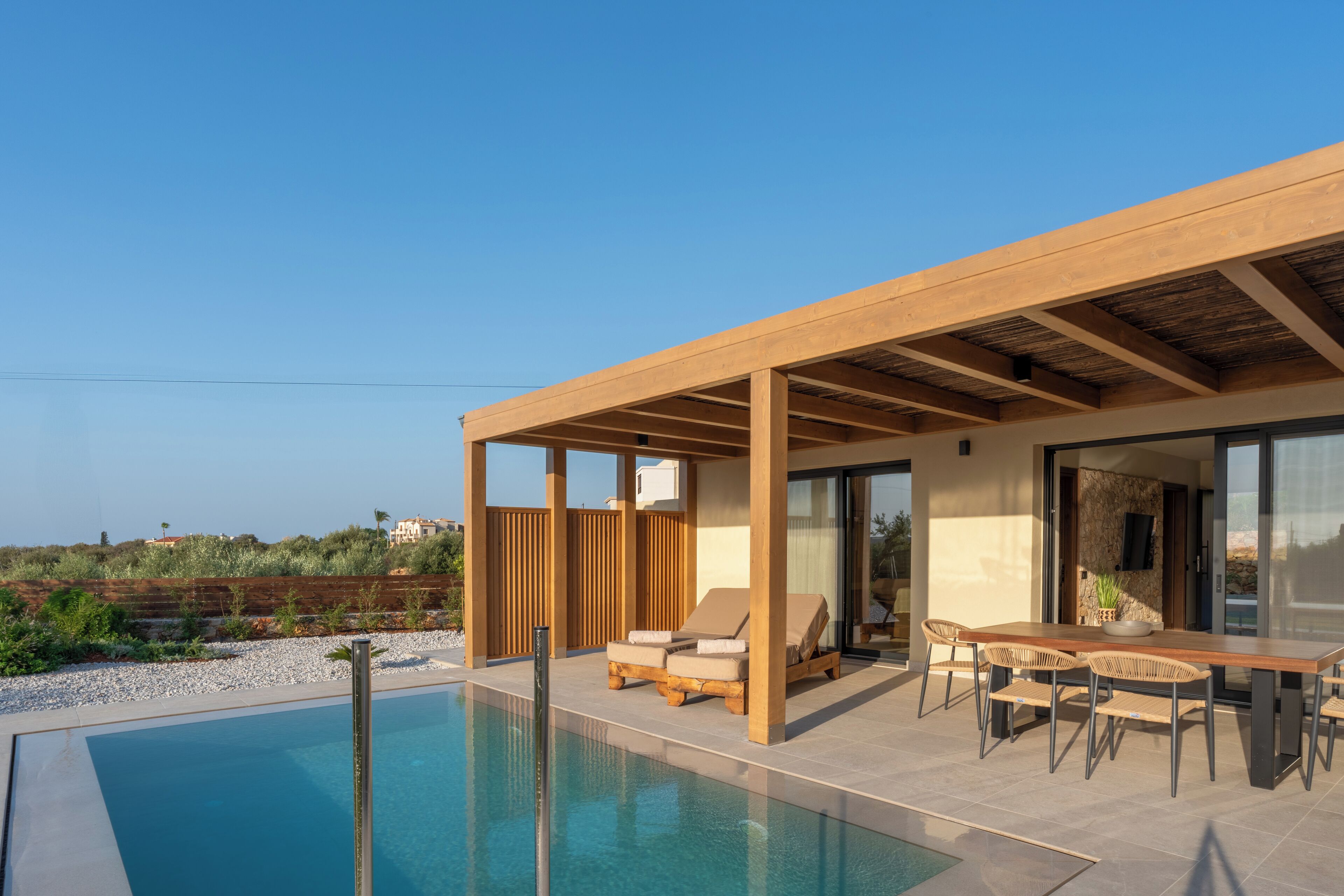 A modern outdoor pool area with a wooden pergola, lounge chairs, and a dining table.