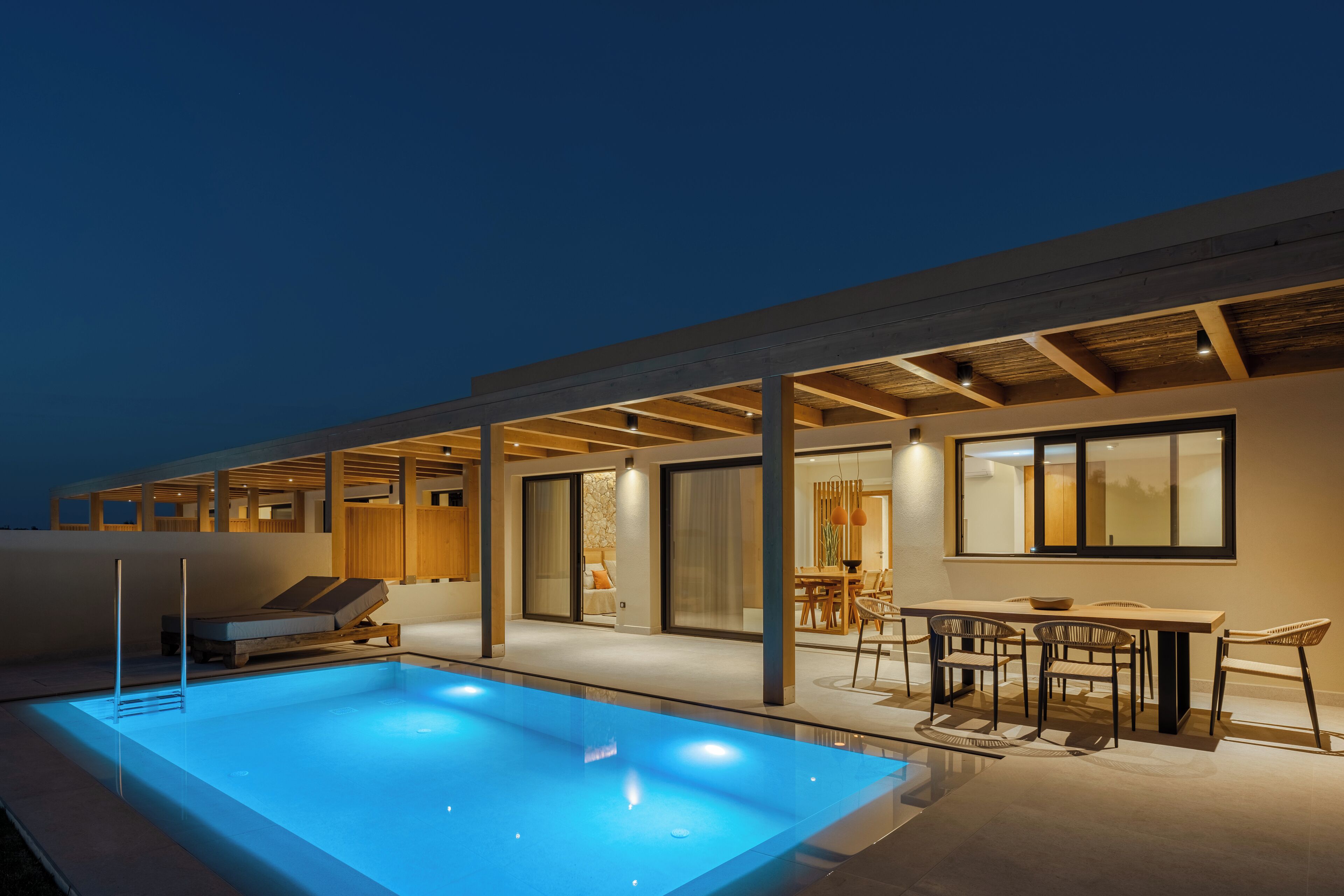 A modern outdoor pool area with a dining setup and a lounge chair.