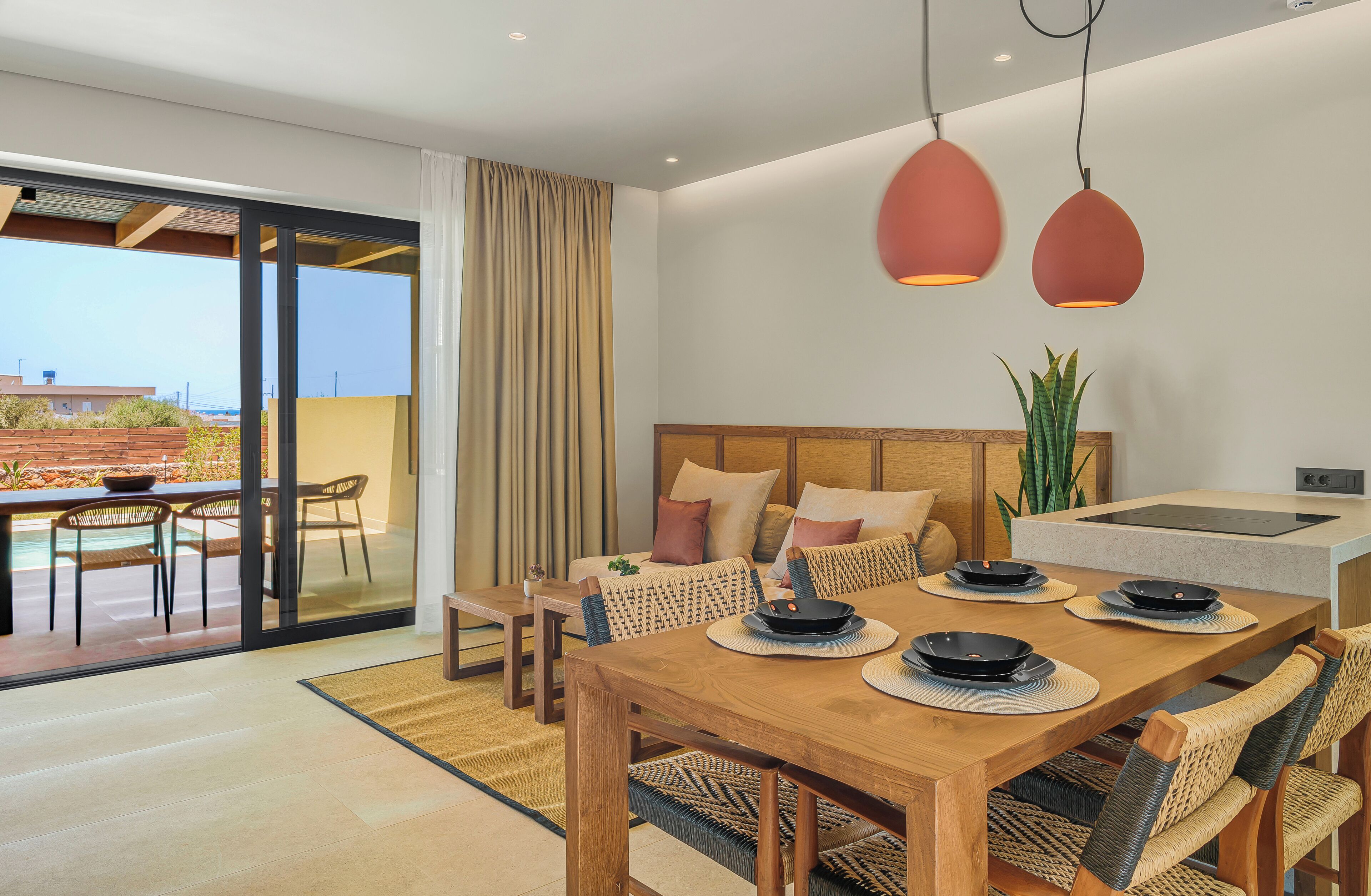 A modern dining area with a wooden table, woven chairs, and a view of a pool through glass doors.