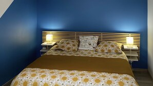 Un dormitorio con techo inclinado, una cama con ropa de cama estampada, dos lámparas de noche y un colgante.