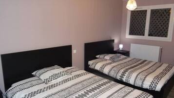 A bedroom with two beds, a nightstand, and a window with blinds.