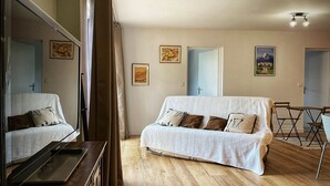 Una habitación con sofá blanco, suelo de madera, una mesa de comedor con sillas y un espejo grande.