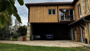 Una casa de madera de dos pisos con un garaje, un coche a la vista y una señal de stop al fondo.