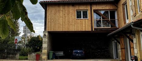 A two-story wooden house with a garage, a visible car, and a stop sign in the background.