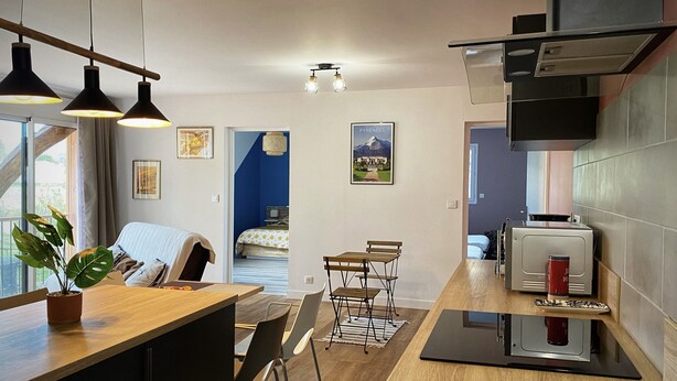 Una cocina moderna con encimeras de madera, un comedor con mesa y sillas, y vistas hacia un dormitorio con cama y pared azul.