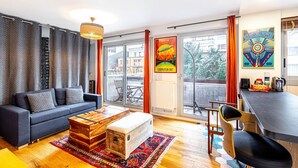 A modern living room with a sofa, coffee table, and a dining area with chairs and a table. - GuestReady - Energetic City Dwelling (Paris)