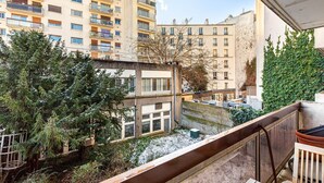 A residential building with multiple balconies, a courtyard with snow, and surrounding greenery. - GuestReady - Energetic City Dwelling (Paris)