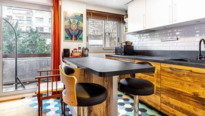 A modern kitchen with a black countertop, wooden bar stools, and a large window with a view of buildings. - GuestReady - Energetic City Dwelling (Paris)