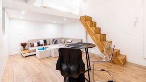 Un salon moderne avec un escalier en bois, un ensemble de canapés, une table basse et un fauteuil transparent.