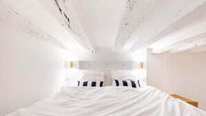 Une chambre à coucher avec un grand lit, des murs blancs et des poutres apparentes.