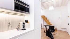 Une cuisine moderne équipée d’un four à micro-ondes encastré, d’une machine à café et d’un bloc à couteaux. Un escalier en bois mène à une autre pièce.