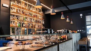 Eine Bar mit Regalen voller Spirituosenflaschen, einer Theke mit Gebäck und hängenden Pendelleuchten.