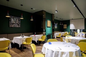 Un comedor con mesas redondas, sillas amarillas y obras de arte en las paredes.