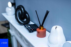 Un estante blanco con un control remoto, auriculares negros y un difusor blanco.