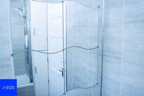 A modern bathroom with a glass shower enclosure, a visible door, and a tiled wall. - 3 Bed House Sleeps 7 With Garden and Parking (Walsall)