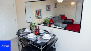 A dining area with a table set for four, a large mirror reflecting the room, and a red carpet. - 2ndhomestays-west Bromwich- 2-bedroom Maisonette (West Bromwich)