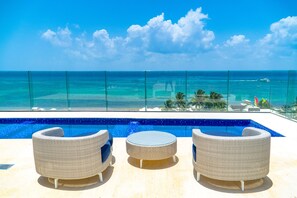 Área da piscina com mobiliário de vime e vista para o oceano.