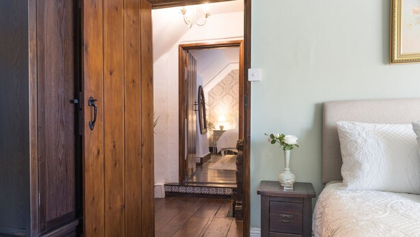 Una camera da letto con un'armadio in legno, un comodino con un vaso e un letto con testiera trapuntata.