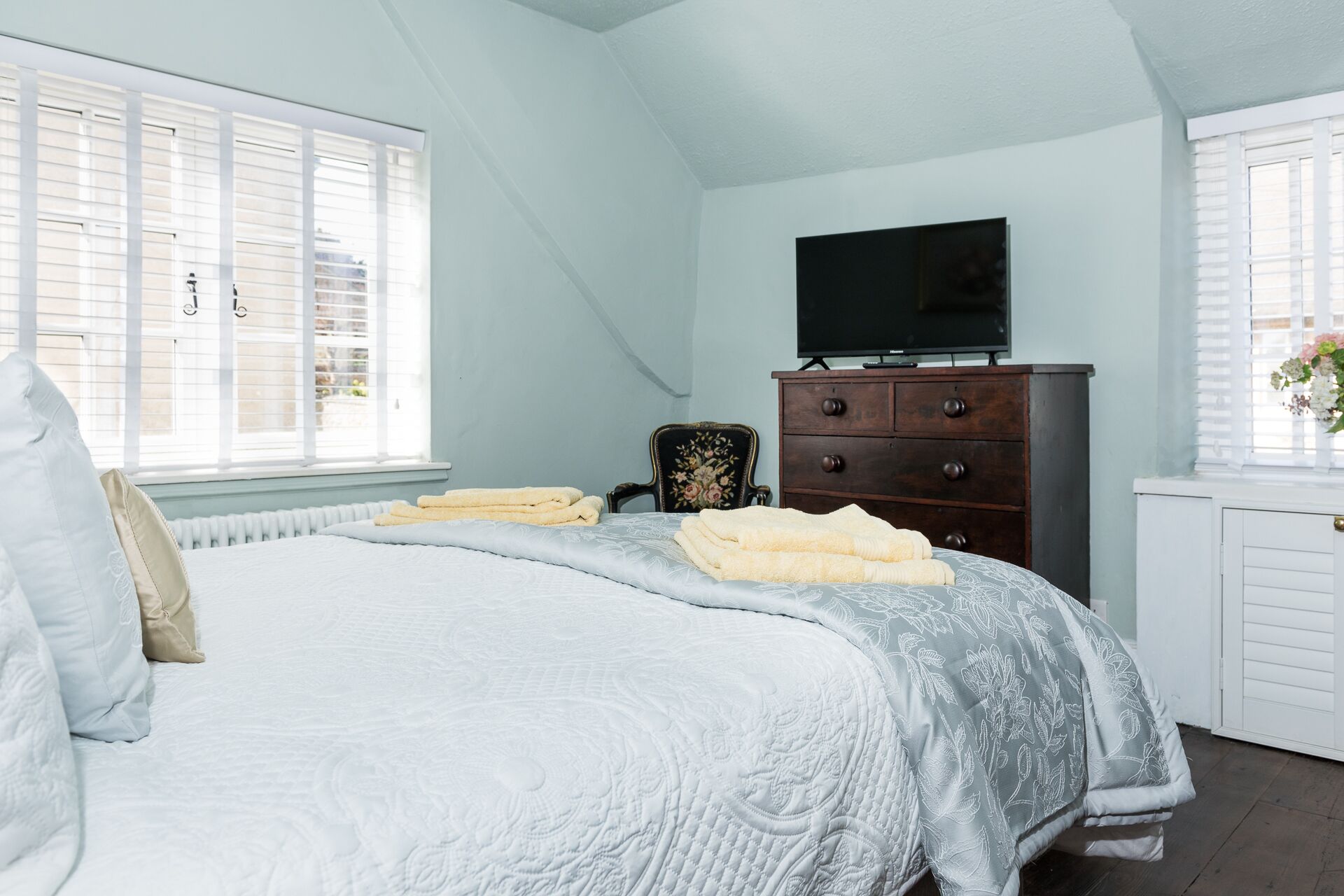 A bedroom with a bed, a dresser, a television, and a window with blinds.