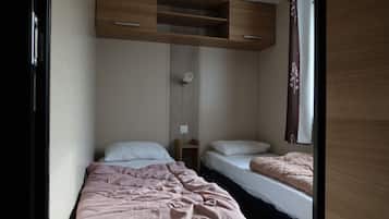 A compact bedroom with two single beds, a wooden shelf unit above the beds, and a small bedside table.