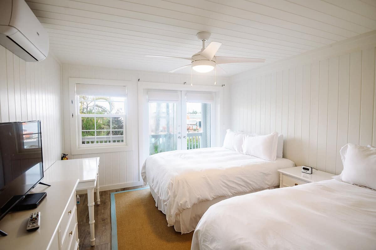 A hotel room with two beds, a TV, a desk, and a ceiling fan.