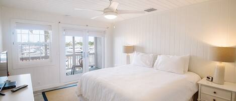 Dormitorio con decoración blanca, que incluye una cama, lámparas de noche, un escritorio y vistas al exterior a través de una puerta corrediza.