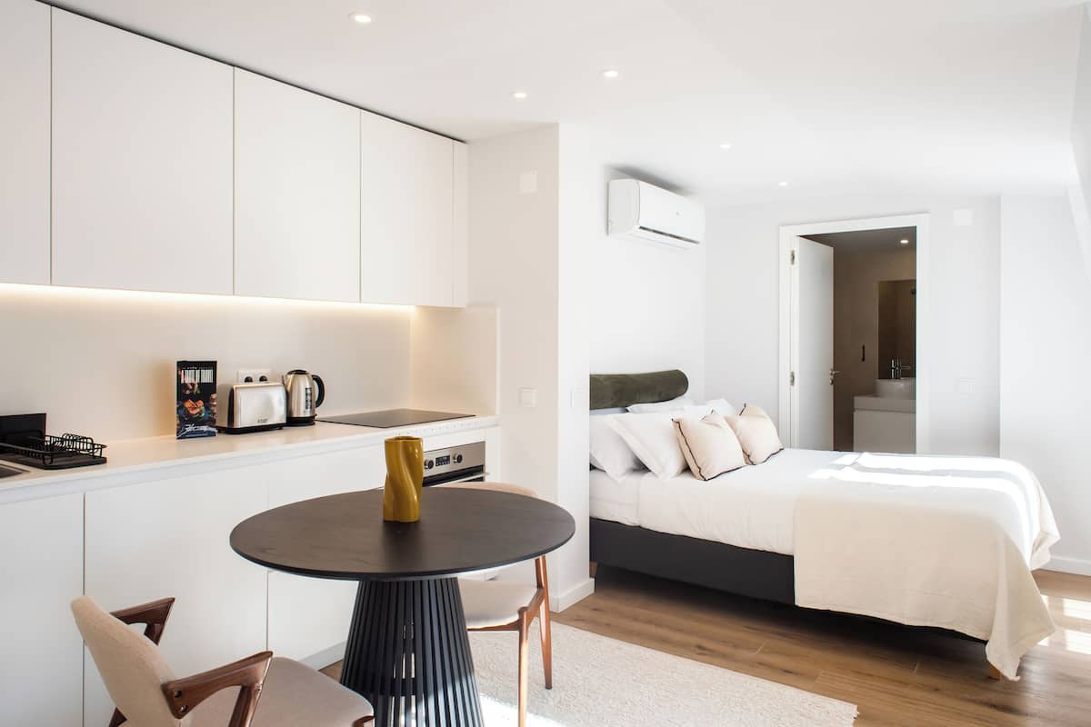 Une chambre moderne et compacte, comprenant un lit, une table de chevet et un petit coin cuisine.