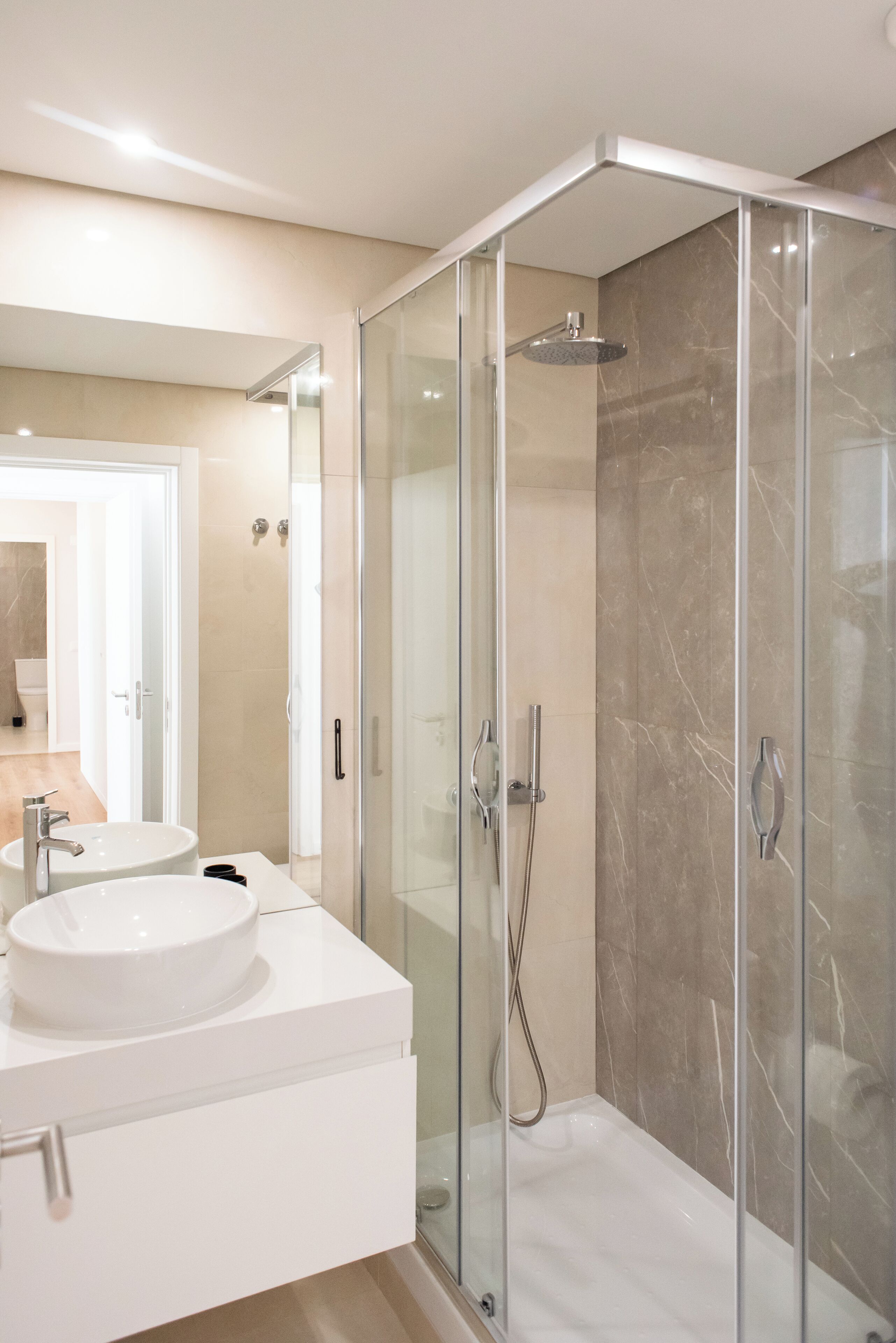 Un baño moderno con ducha de vidrio, lavamanos blanco y pared de ducha con mosaicos de mármol.