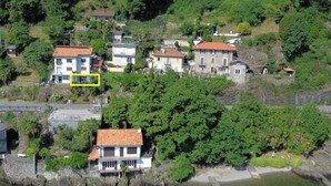 A coastal village with houses built on a hillside, a clear view of the sea, and a stone bridge.
