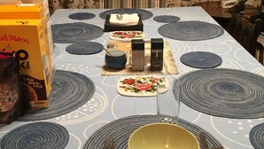Una mesa de comedor dispuesta con manteles individuales, platos, tazones, cubiertos y una caja de cereal.