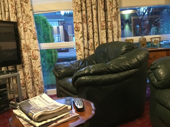A living room with a leather armchair, a television, and a window with curtains. - Lowry House Hotel in Walsall (Birmingham)