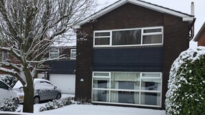 Una casa de dos pisos con un garaje, rodeada de tierra y árboles cubiertos de nieve.