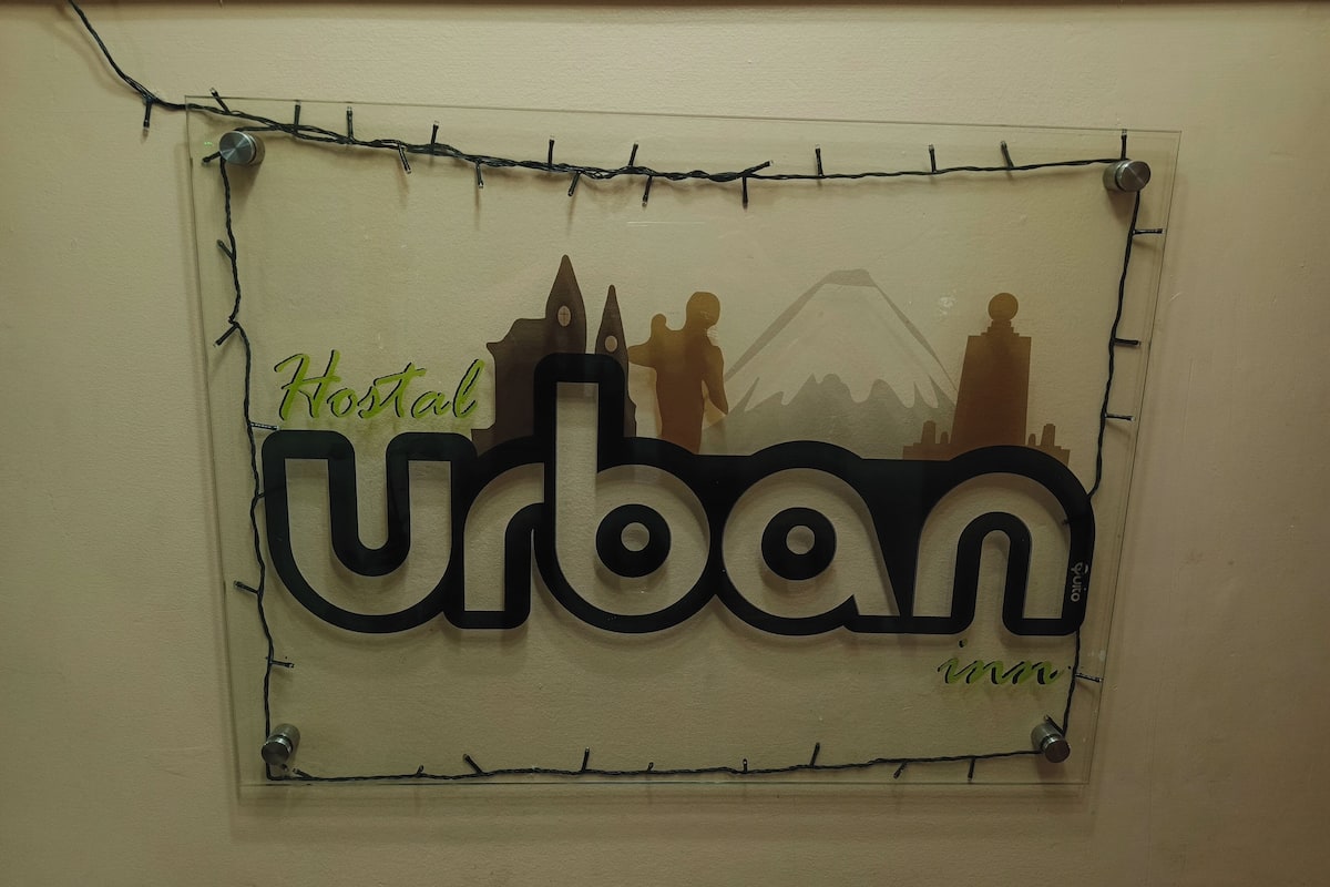 A sign with the word "Urban" and silhouettes of buildings, including a church and a mountain, with the text "Hostal Urban" on a beige wall.