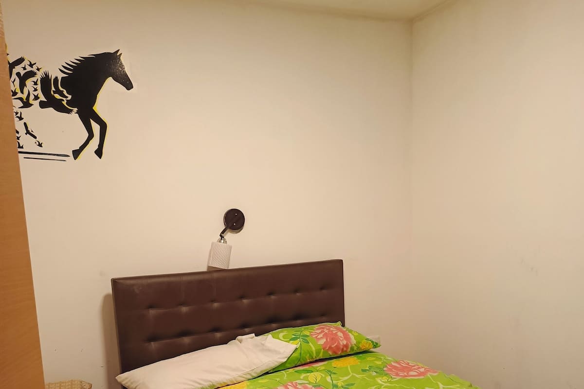 A bedroom with a bed, a nightstand, a wall decoration, and a door.