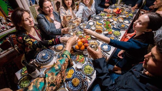 A group of people around a table with various dishes and drinks, suggesting a social gathering or meal.
