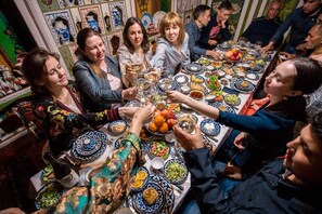Un groupe de personnes est réuni autour d’une table, où l’on voit différents plats et boissons, ce qui laisse supposer qu’il s’agit d’un événement social ou d’un repas.