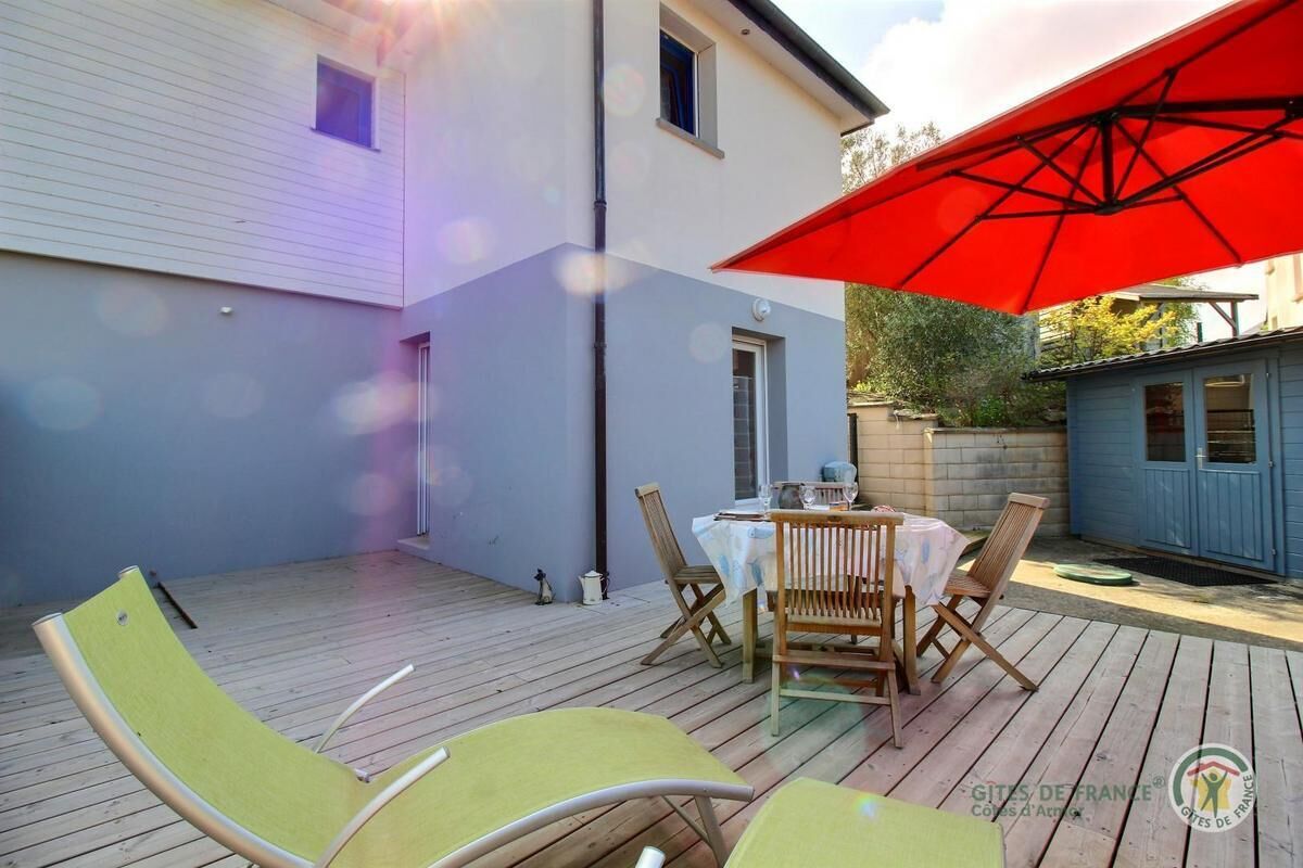 Een terras met een tafel, stoelen en een rode parasol, plus een houten terras.